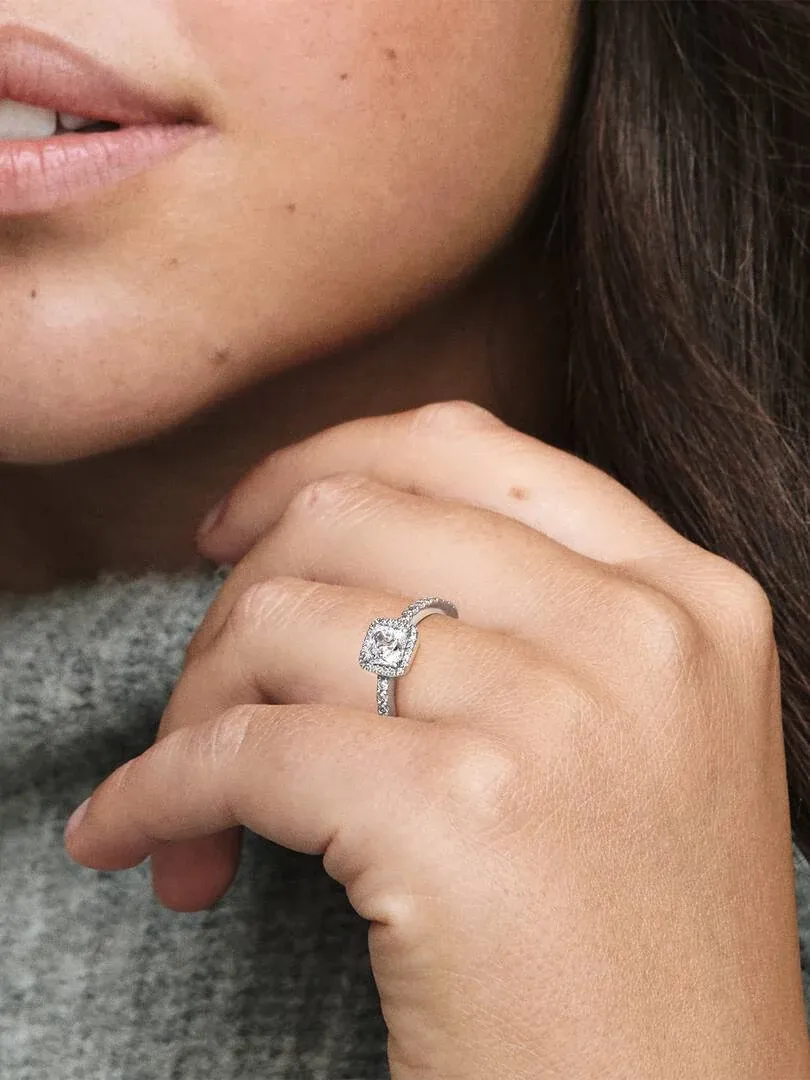 Close-up van de ring met vierkante steen aan een vinger, zijaanzicht tegen een grijze achtergrond.