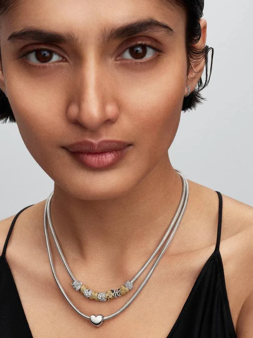 Close-up of necklace with charms on a model's neck, neutral background and soft lighting.