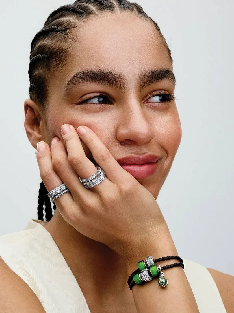 Nahaufnahme einer Hand am Gesicht, die silberne Ringe und ein Lederarmband mit Charms zeigt.