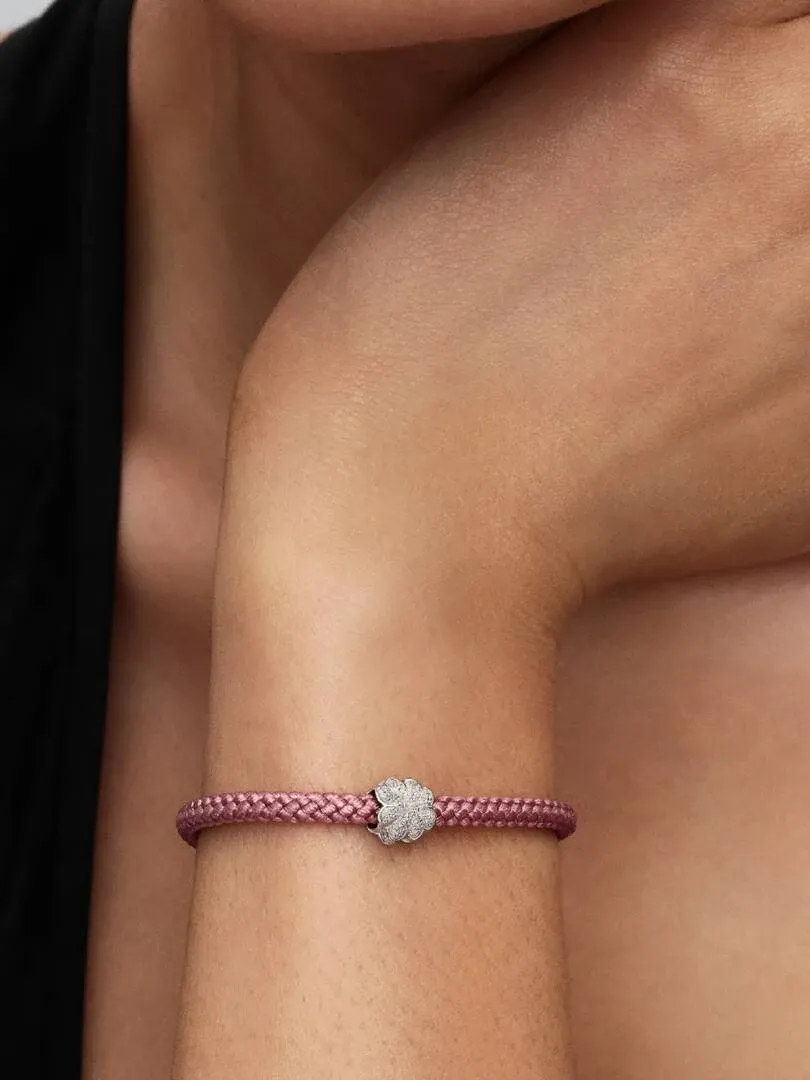 Primer plano del charm de trébol en una pulsera trenzada rosa, puesto en la muñeca.