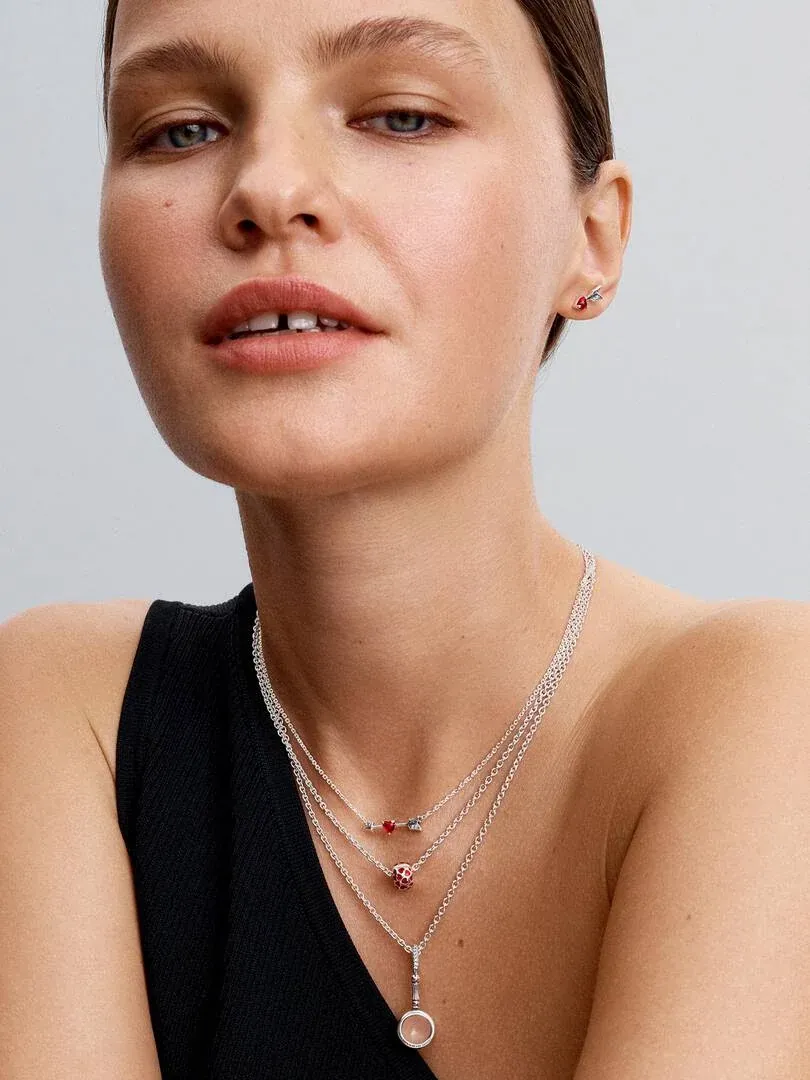 Gros plan de colliers superposés avec charms rouges portés par un modèle, vue de face.