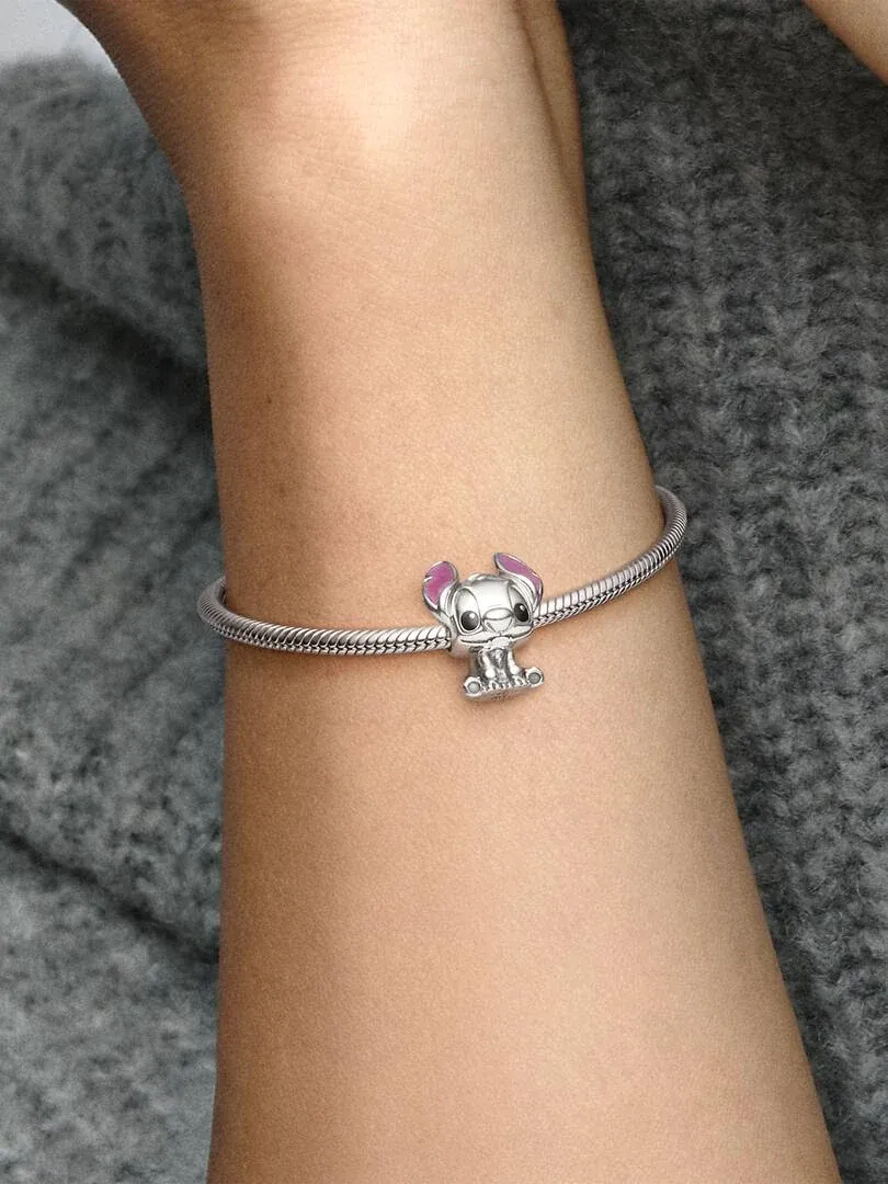 Primer plano del charm de Stitch en una pulsera de plata, puesto en la muñeca sobre fondo gris texturizado.
