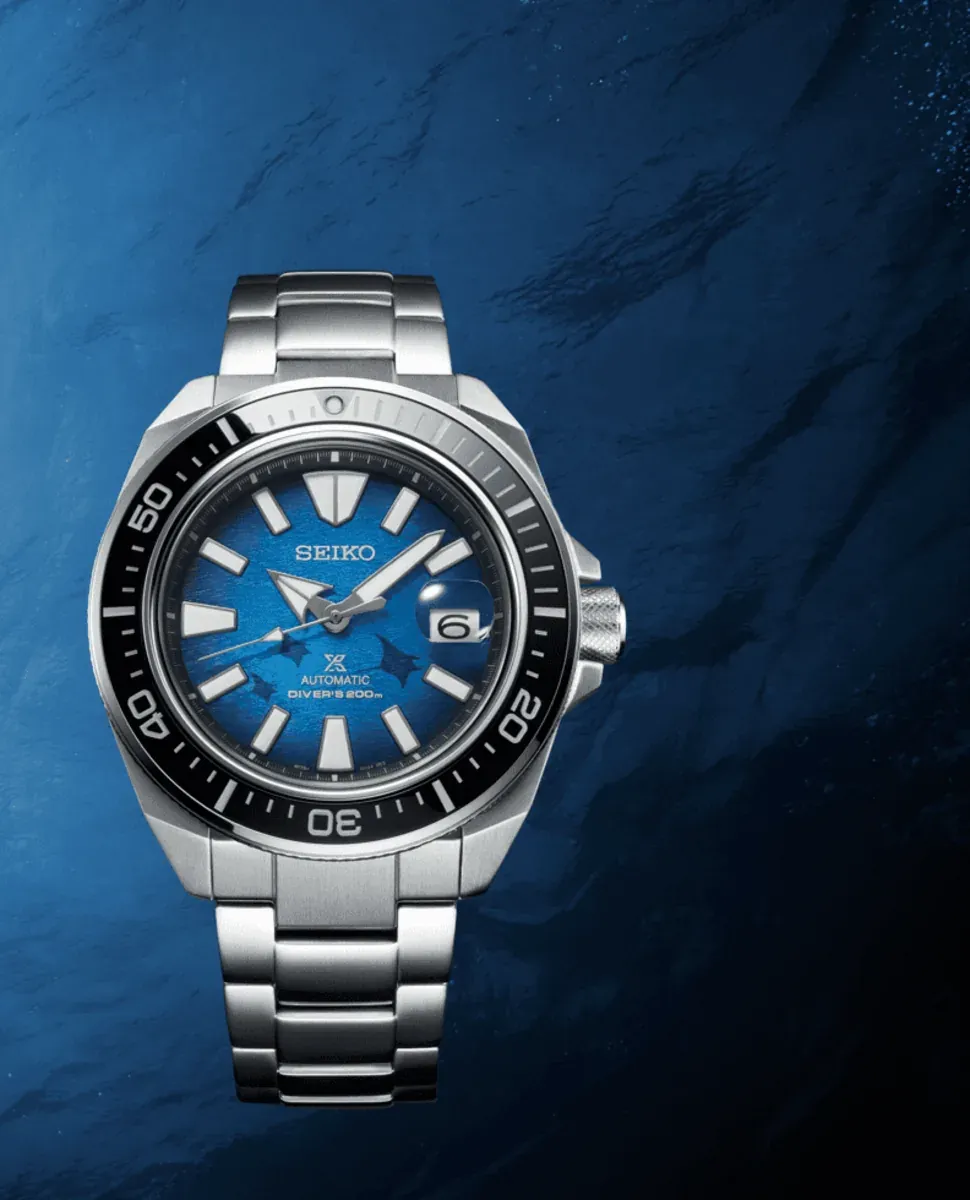 Vista frontal del reloj sobre fondo azul con texturas orgánicas que simulan el fondo marino.