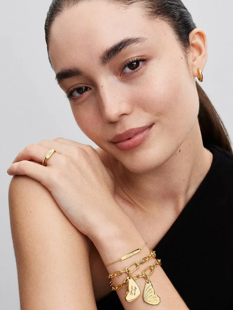 Primer plano de modelo con anillo de barra dorado en el dedo y pulseras a juego, fondo neutro.