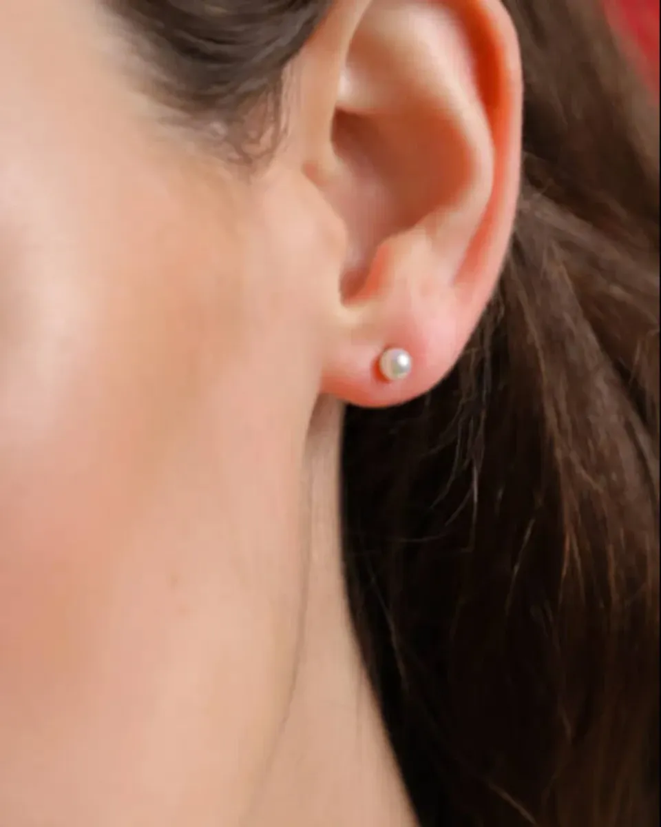 Close-up side view of a white pearl stud earring worn on the earlobe, blurred background.