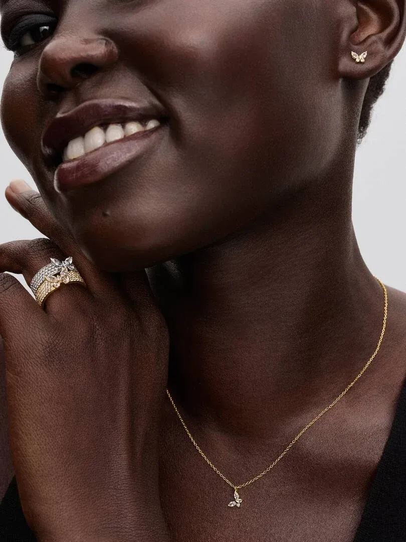 Gros plan d'un modèle portant le collier papillon, des boucles d'oreilles et une bague assortis, fond neutre.