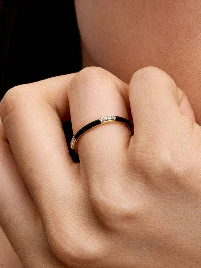 Primer plano del anillo con esmalte negro y circonitas puesto en un dedo, toma lateral sobre piel.