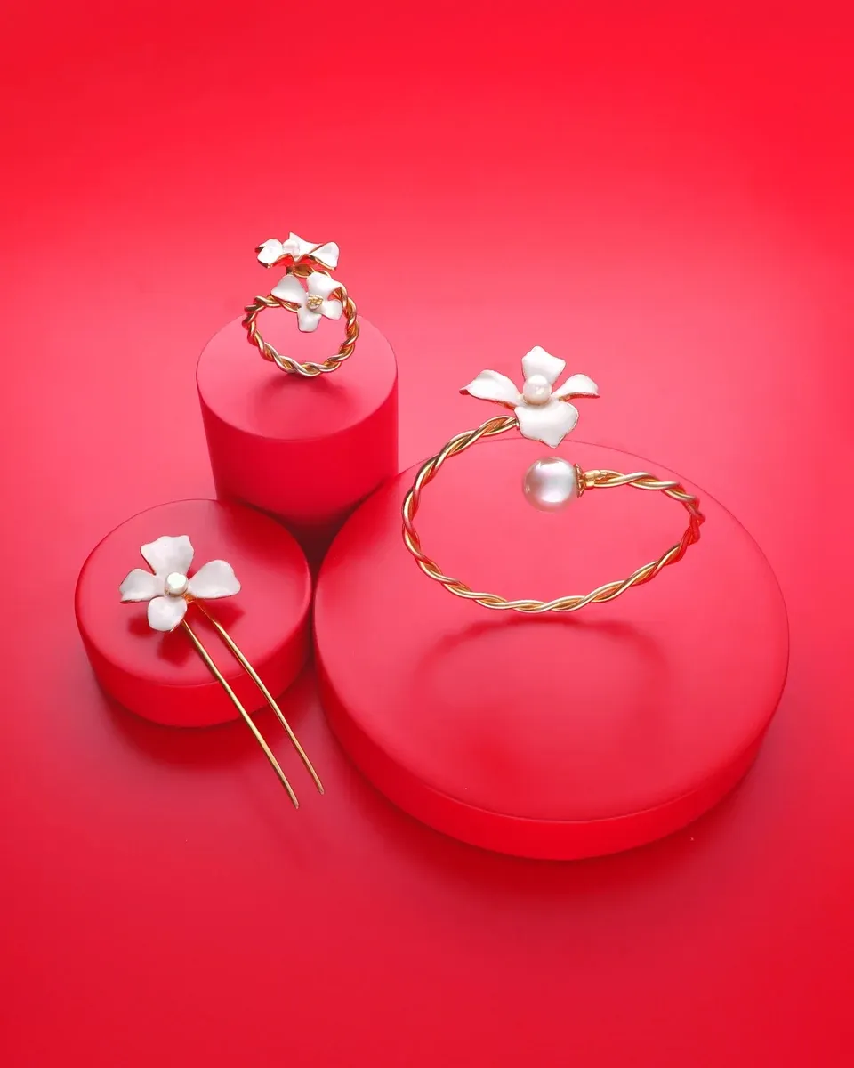 Ensemble de bijoux sur socles rouges : bague, bracelet et boucles d'oreilles avec fleurs blanches et perles.
