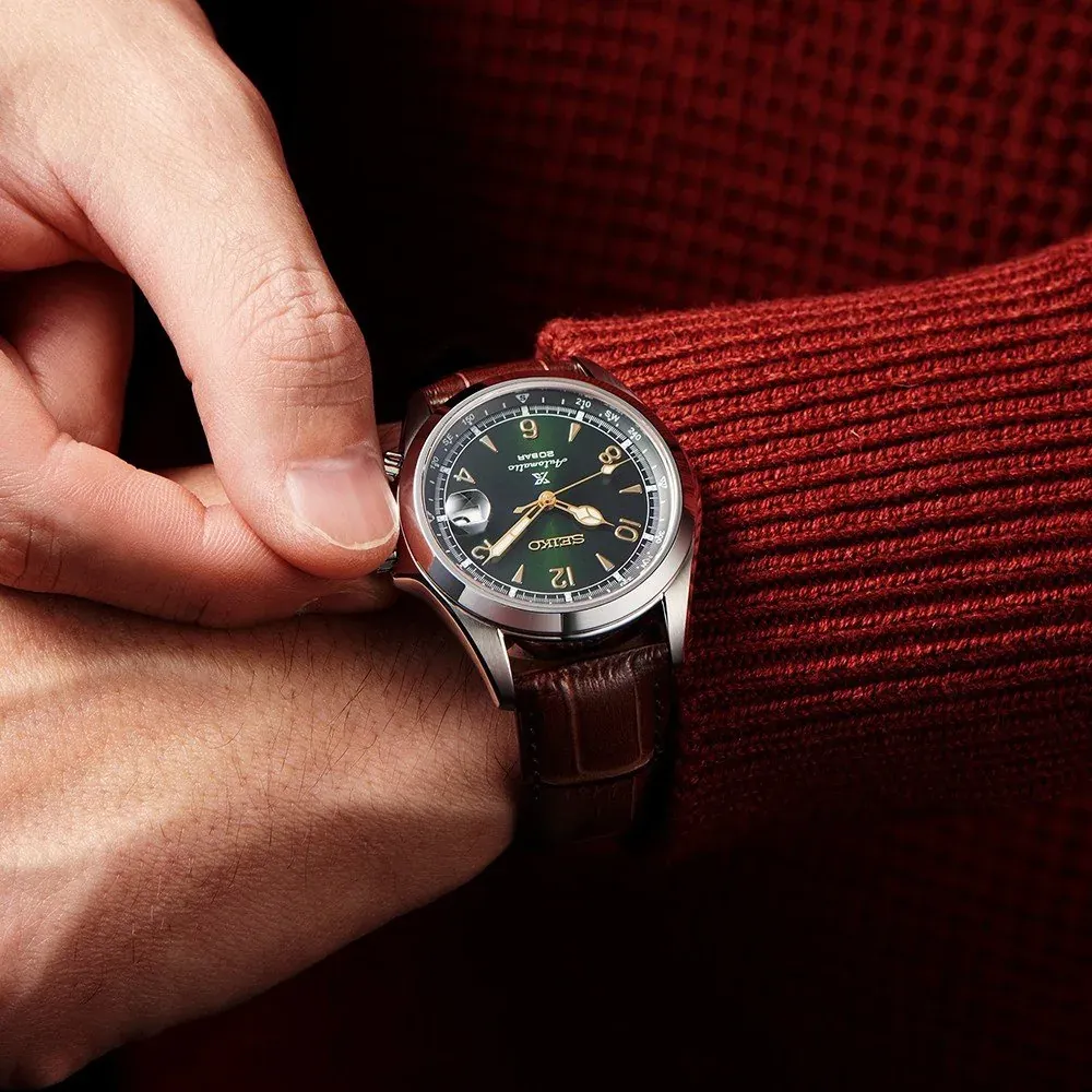 Primer plano del reloj puesto en muñeca, mano tocando la caja, manga de jersey rojo, toma detallada