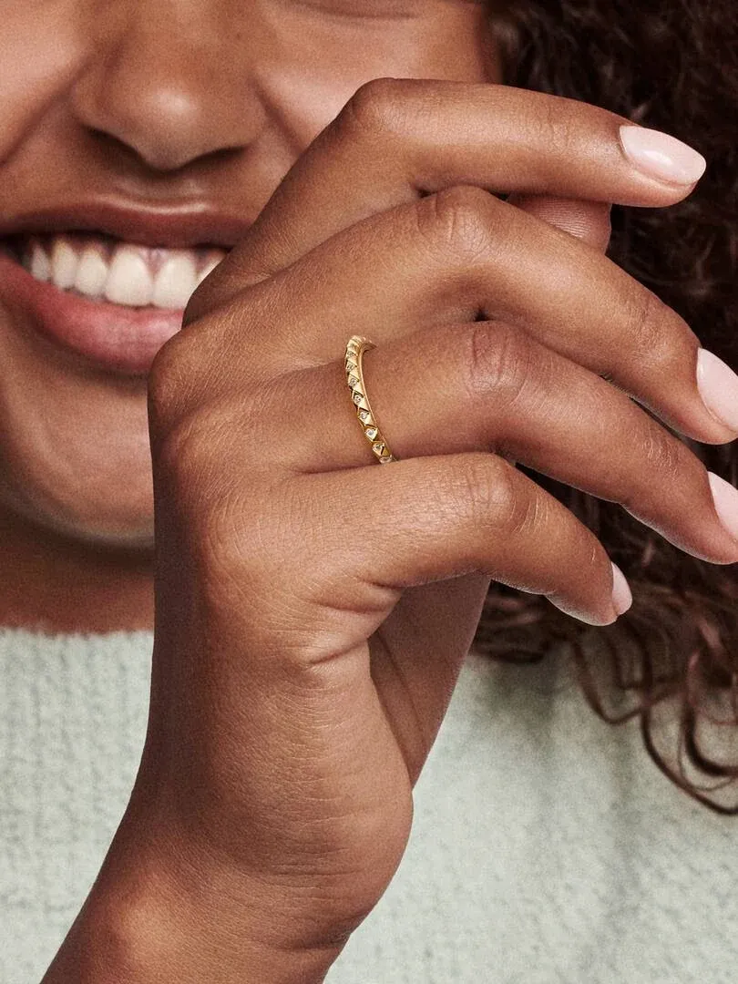 Primer plano del anillo dorado con detalles piramidales puesto en el dedo, mano de modelo sobre fondo desenfocado.