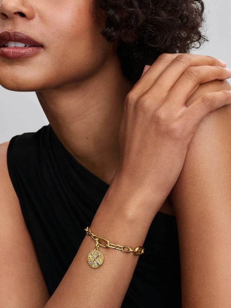 Nahaufnahme des Medaillon-Charms an einem goldenen Armband am Handgelenk, dunkler Hintergrund.