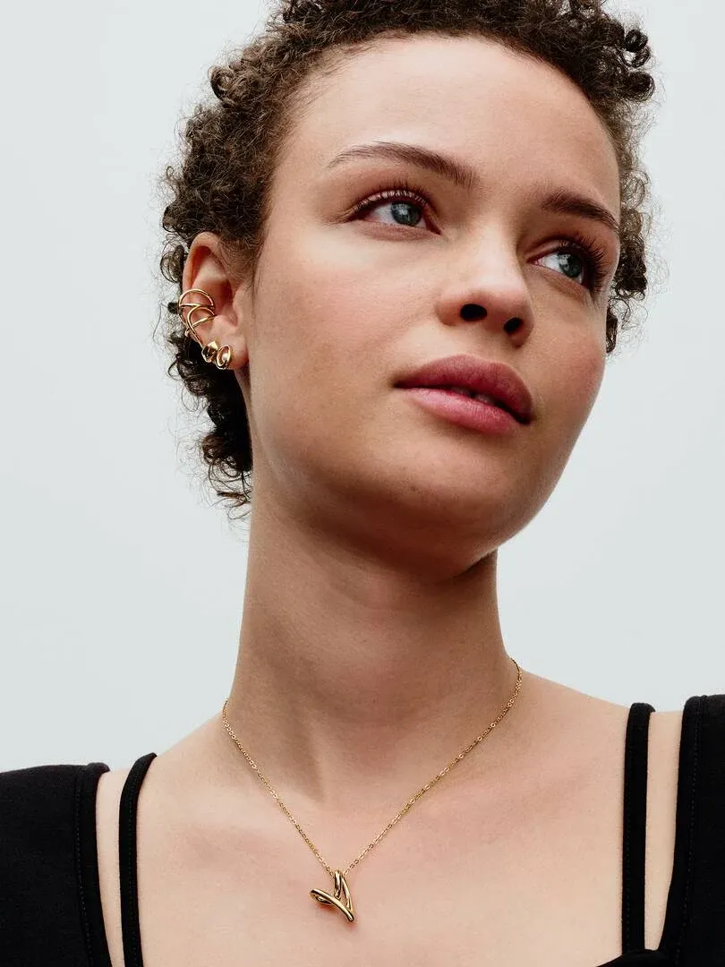 Close-up of model wearing gold heart necklace and matching earrings against a light neutral background.