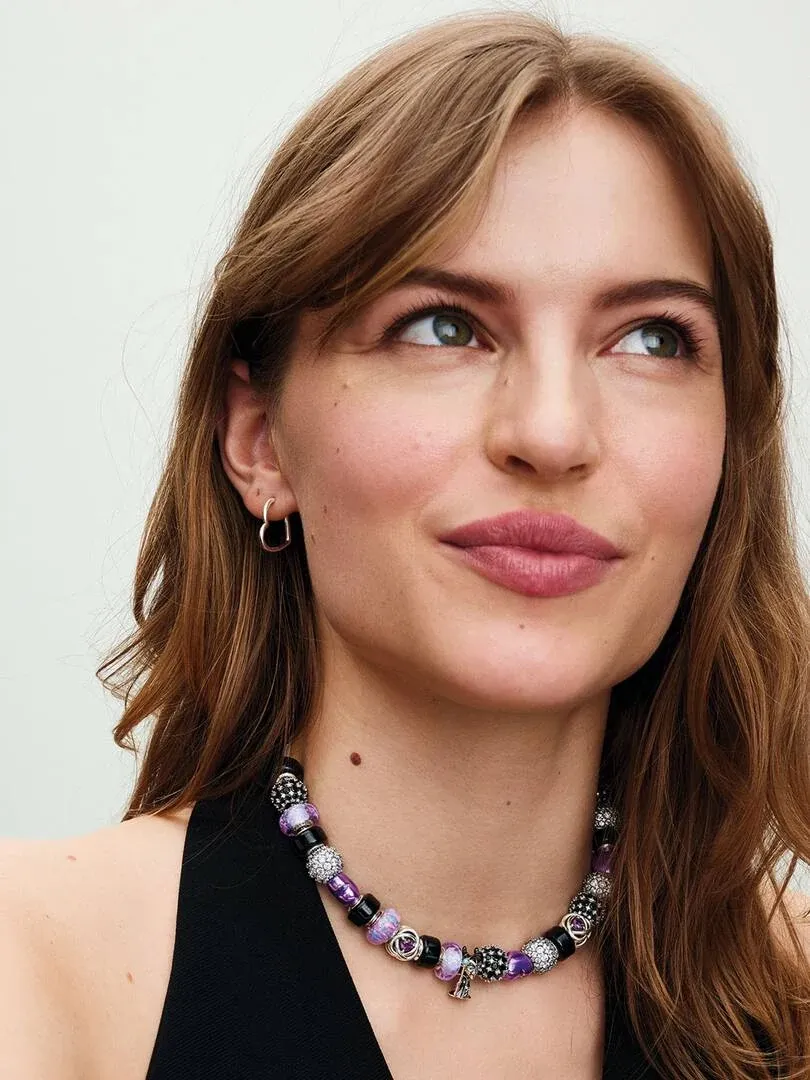 Gros plan de profil d'un modèle portant des créoles en argent et un collier de perles violettes.