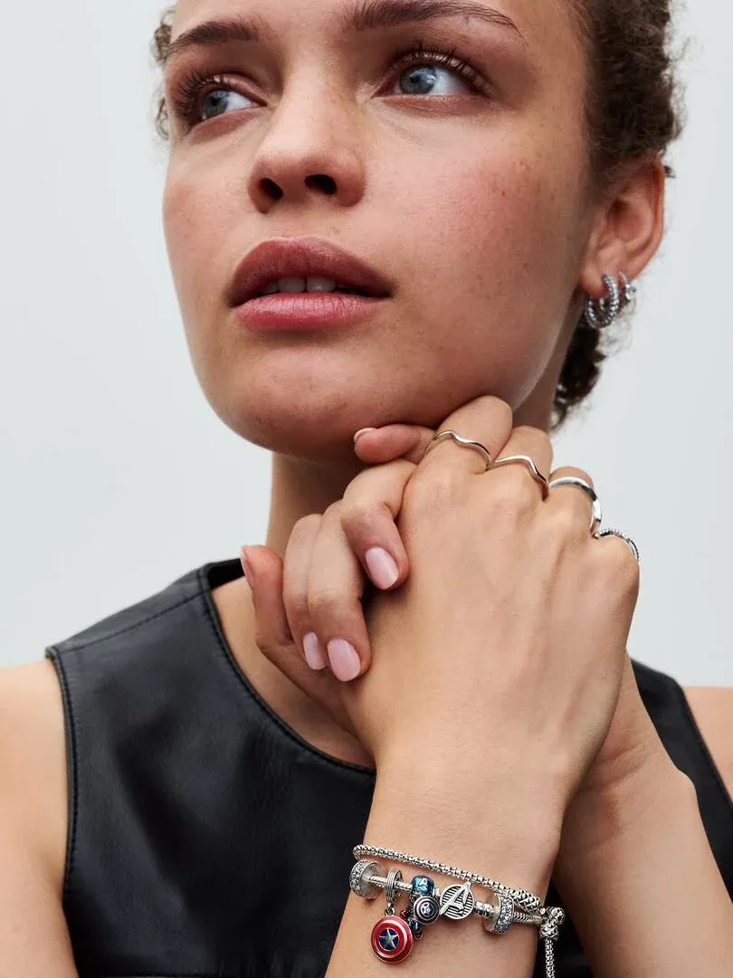 Gros plan du poignet avec bracelet à charms, mains près du visage sur fond neutre.