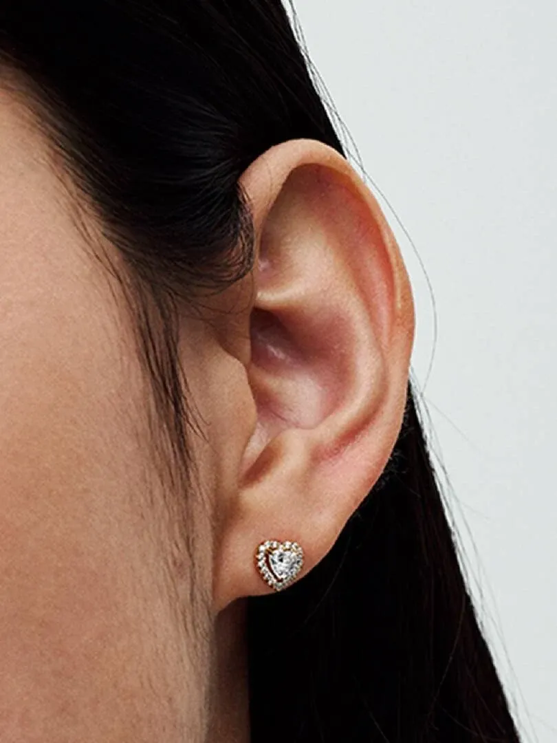 Gros plan latéral d'une boucle d'oreille puces en forme de cœur portée sur le lobe, fond neutre.