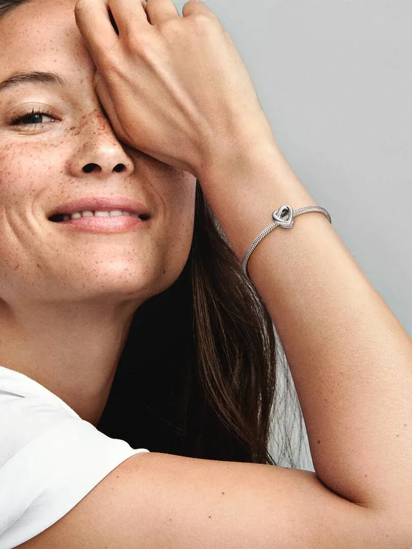 Close-up van een vrouw met de hartknoop charm om haar pols, zijaanzicht tegen een neutrale grijze achtergrond.