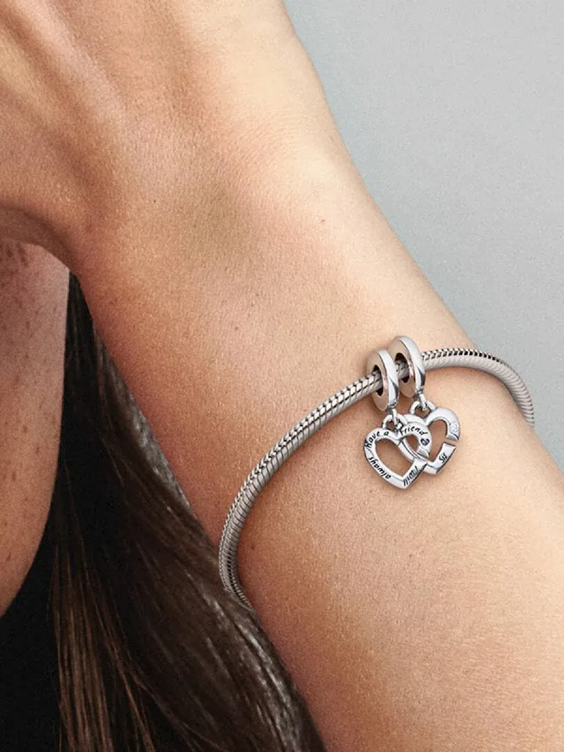 Primer plano de charm de corazones en pulsera de plata, puesto en la muñeca con fondo desenfocado.