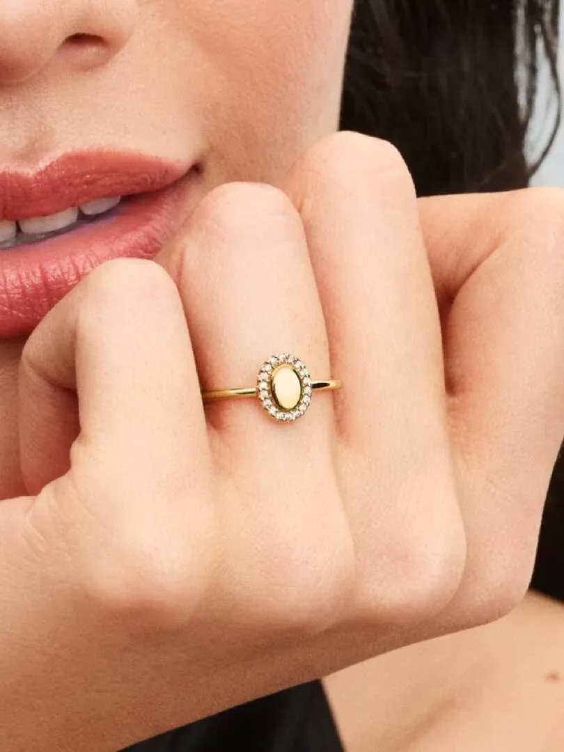 Primer plano del anillo con piedra ovalada en un dedo, toma lateral con rostro de modelo desenfocado al fondo.