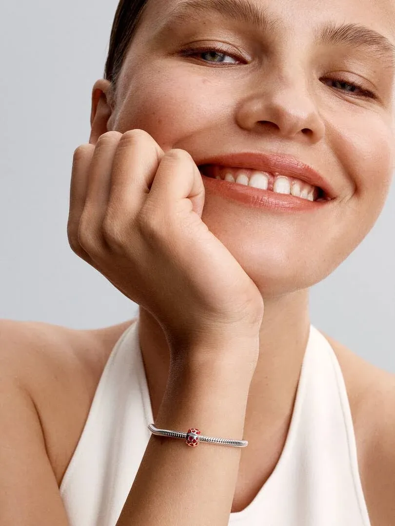 Gros plan du poignet avec le charm cœur, modèle souriant sur fond neutre clair.