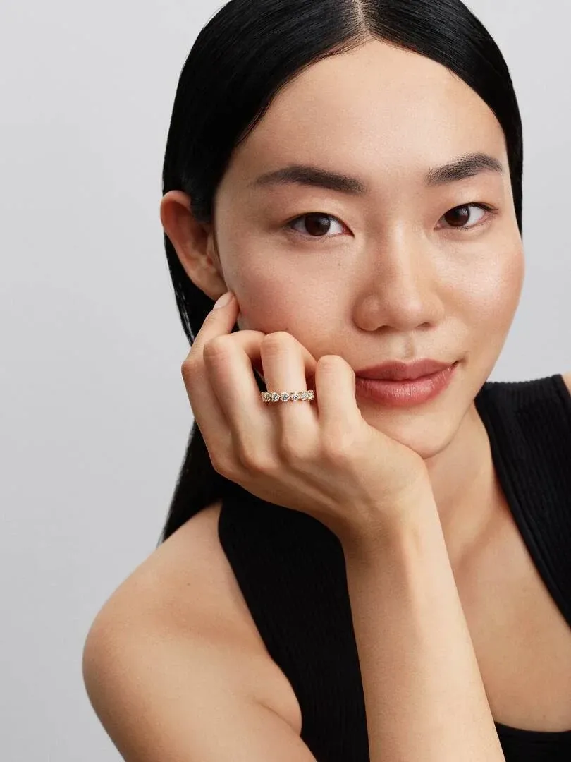 Primer plano de anillo con circonitas en forma de corazón puesto en el dedo, mano apoyada en la barbilla.