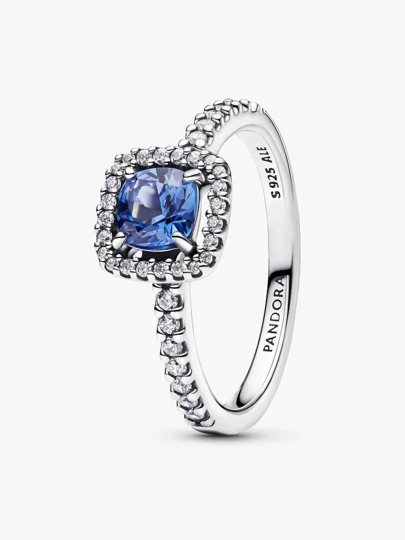 Silver ring with square blue stone and pavé halo, side angle view on a white background.