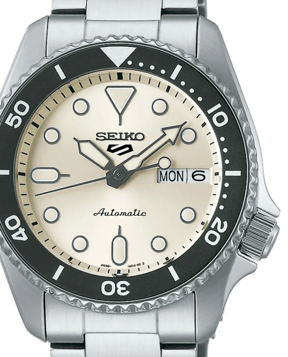 Primer plano frontal de la esfera blanca, el bisel negro y la corona del reloj sobre fondo blanco.