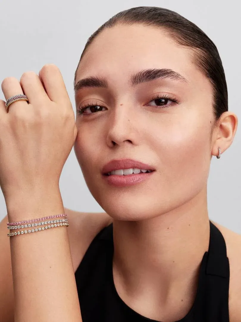 Gros plan d'un modèle portant un bracelet tennis rose et une bague assortie, vue de face sur fond neutre.
