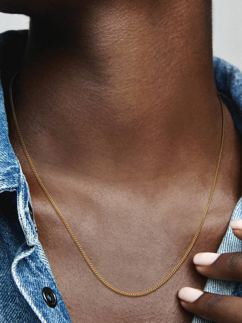 Primer plano del collar dorado sobre el cuello de una modelo, con camisa de denim azul desenfocada.