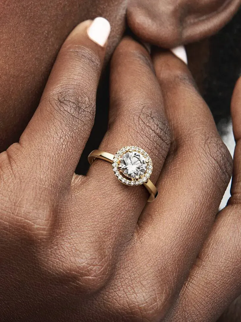 Primer plano del anillo halo con circonitas puesto en el dedo, toma lateral sobre piel.