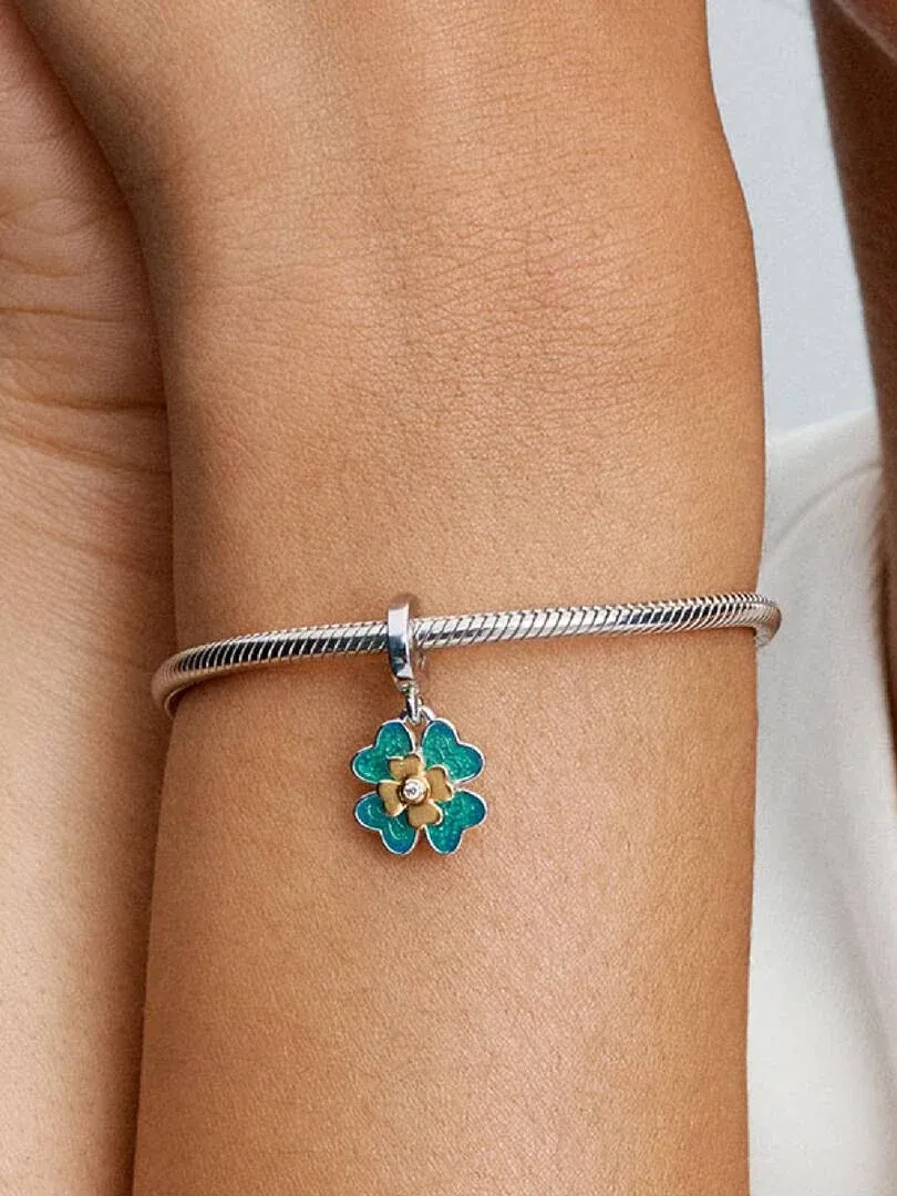Gros plan d'un charm trèfle bleu et doré suspendu à un bracelet en argent au poignet.