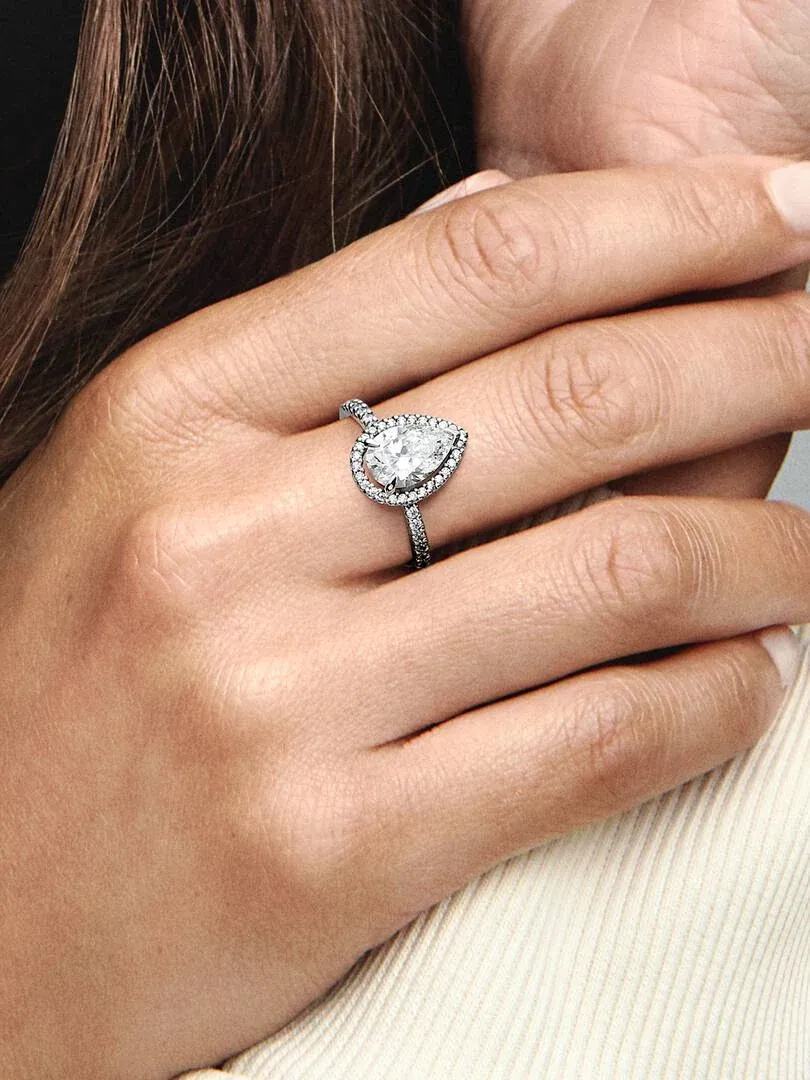 Close-up van de peervormige ring gedragen aan een vinger, zijaanzicht tegen een wazige neutrale achtergrond.