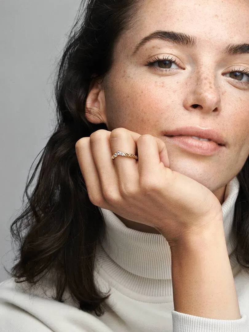 Primer plano de anillo dorado con circonitas en dedo anular, modelo apoyando la barbilla sobre su mano.