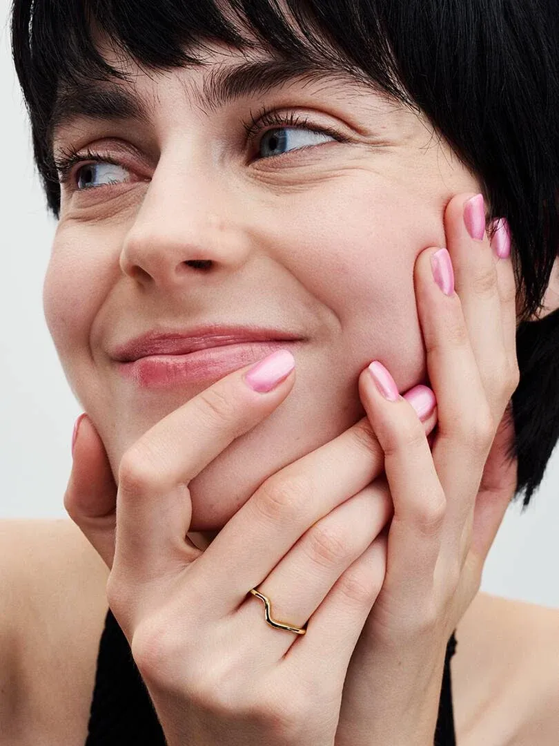 Primer plano de anillo ondulado dorado en dedo anular, manos cerca del rostro de una modelo.