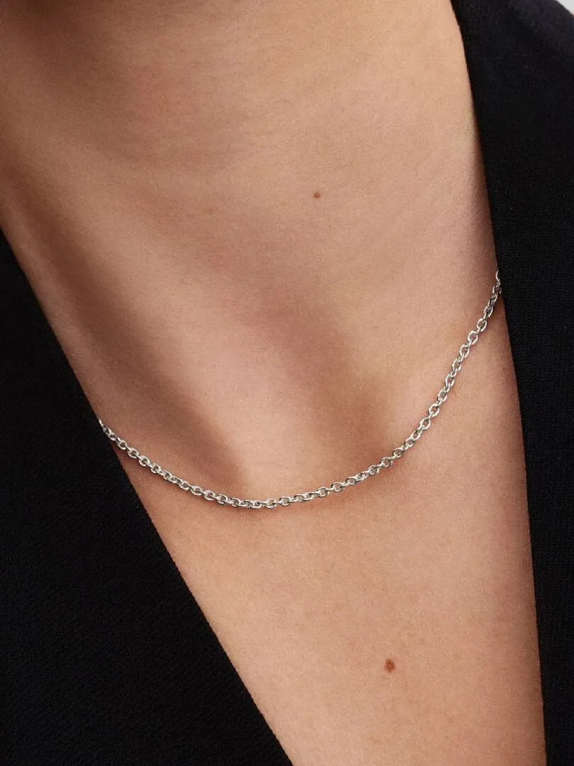 Close-up of the silver chain on the neck and collarbone, side view against a dark background.