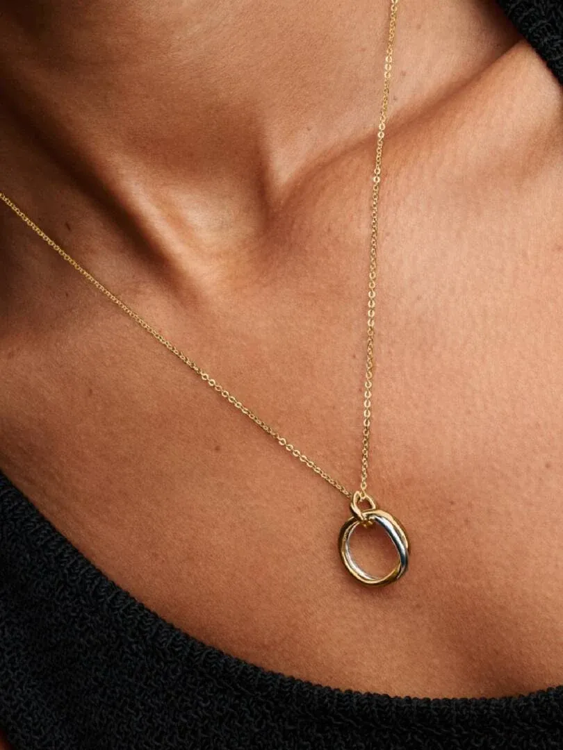 Close-up of the organic pendant necklace on a model's neck, dark blurred background.