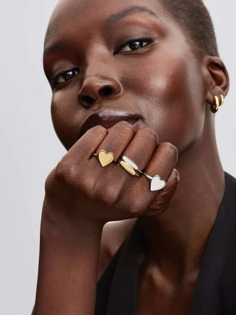 Primer plano de mano con anillos de corazón en dedos, modelo con fondo neutro claro.