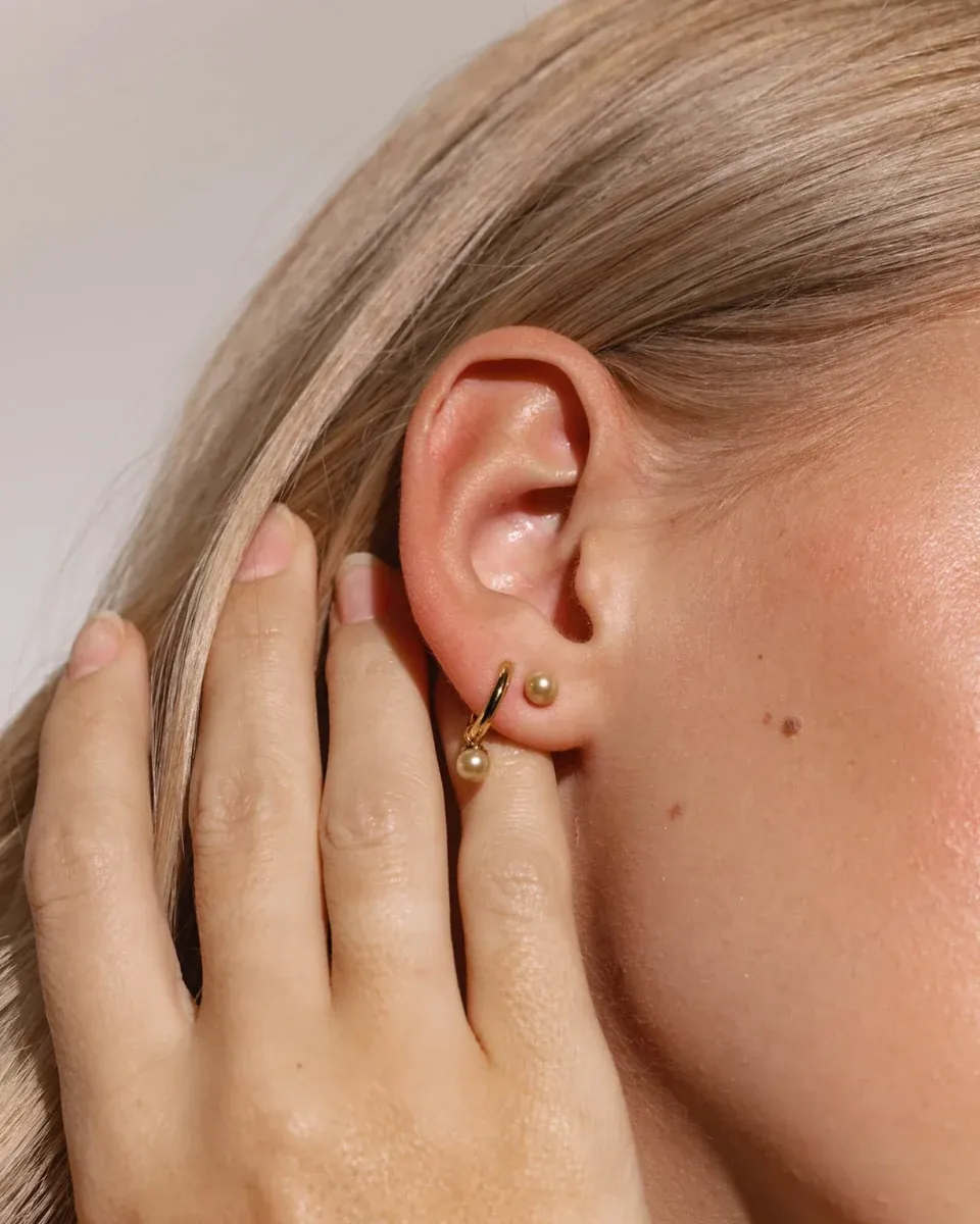 Seitenansicht Nahaufnahme des Mini Hoop Ohrrings mit Champagner-Perle am Ohr.