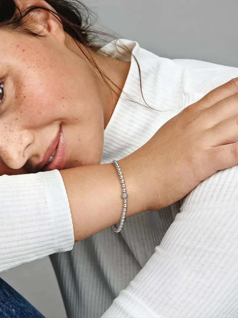 Primer plano de la pulsera de esferas en la muñeca, toma lateral con modelo vistiendo prenda blanca.