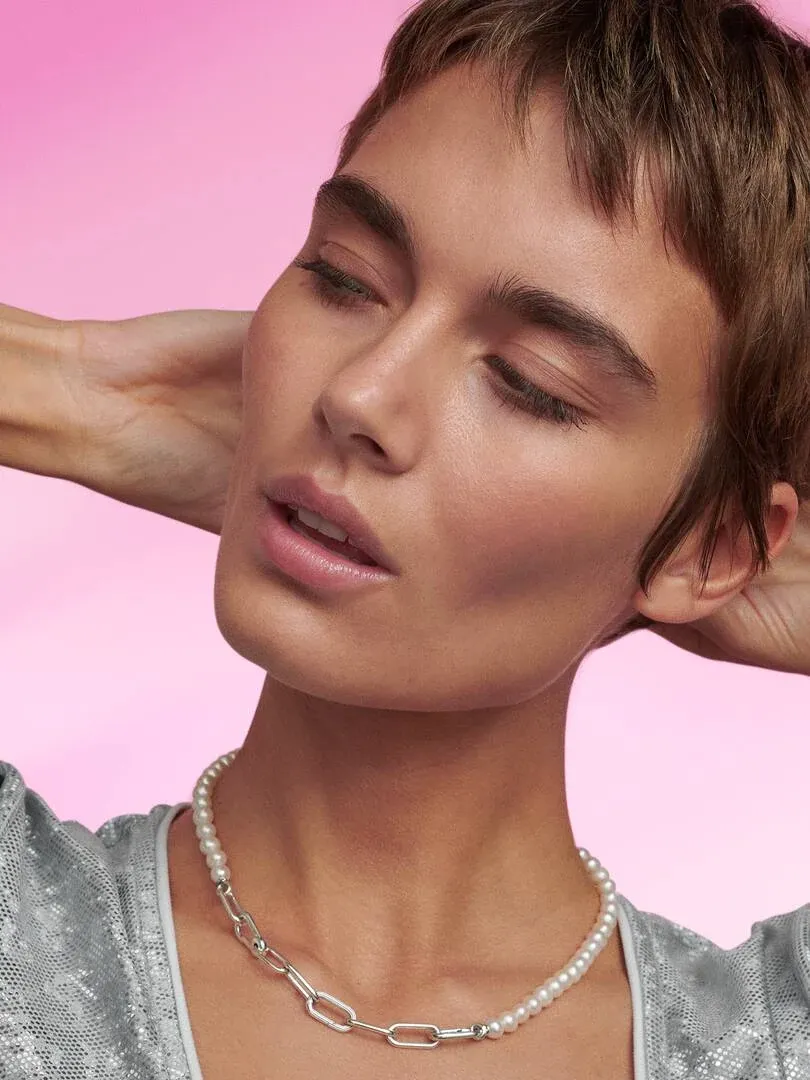 Primer plano del collar de perlas y eslabones sobre el cuello de una modelo, fondo rosa sólido.