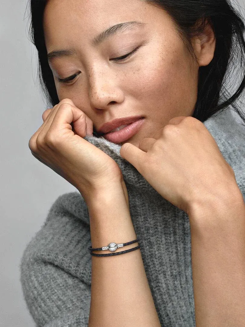 Primer plano de la pulsera de cuero negro en la muñeca, toma lateral con modelo vistiendo jersey gris.