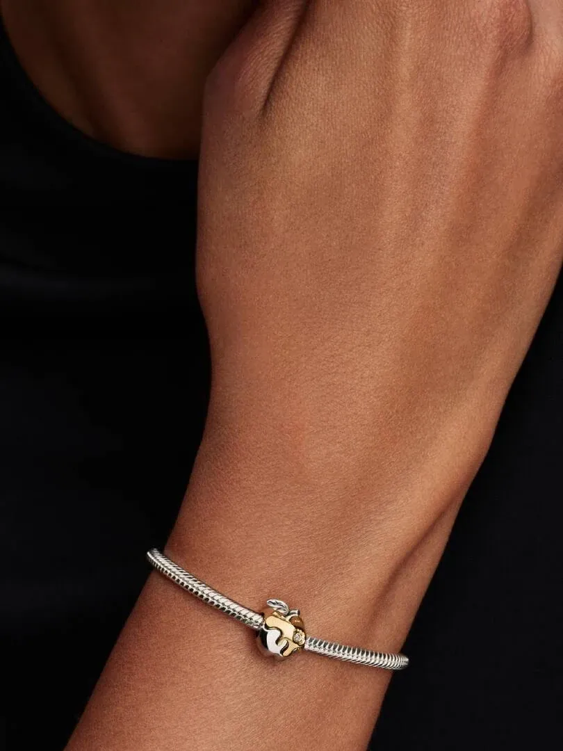 Primer plano del charm de manzana en una pulsera, puesto en la muñeca con fondo oscuro desenfocado.