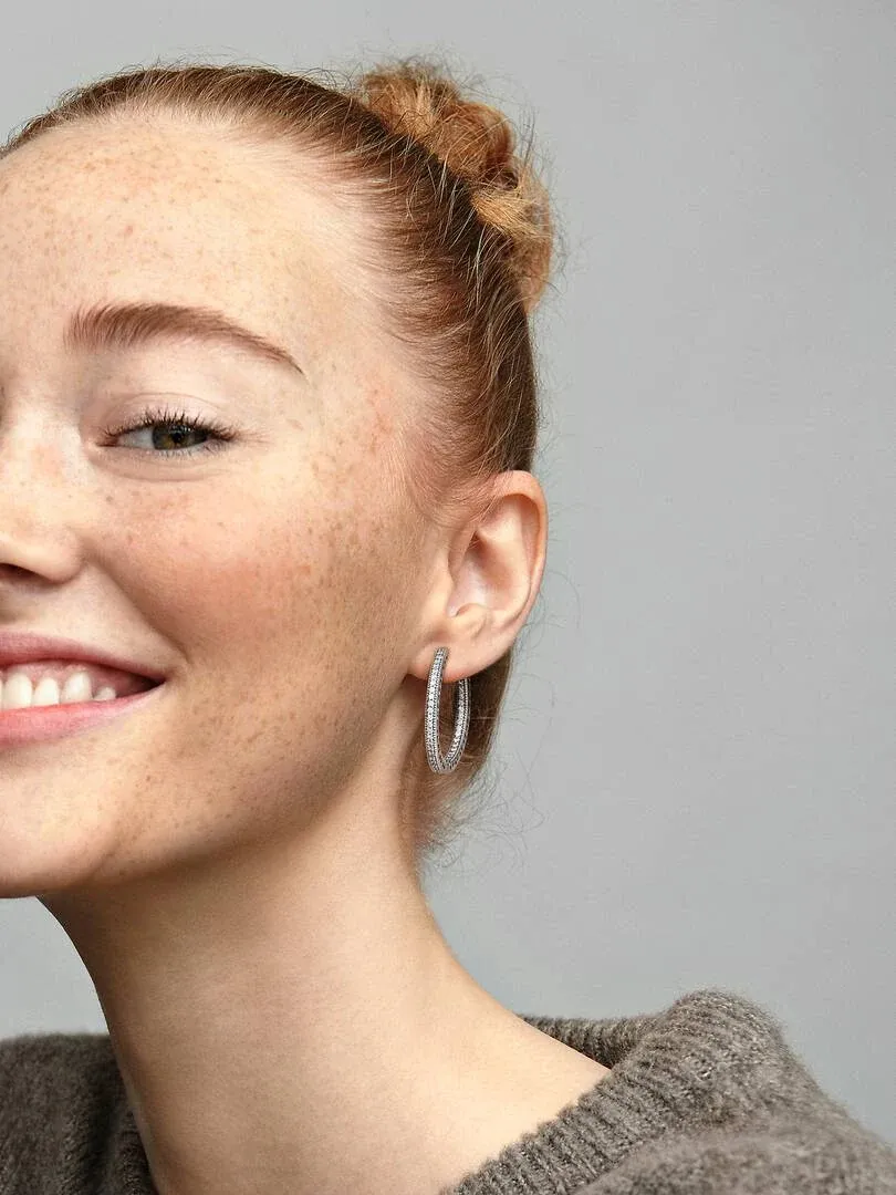 Zijaanzicht close-up van een oorring met zirkonia, gedragen aan het oor van een model tegen een grijze achtergrond.