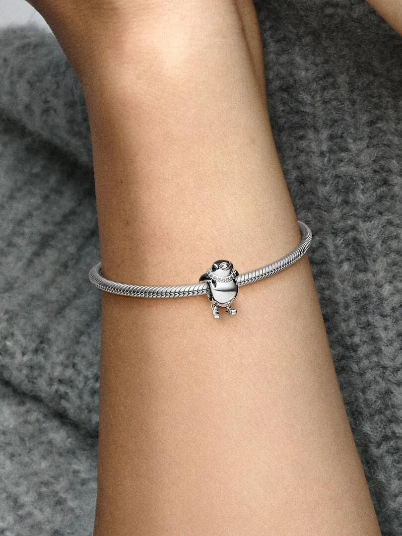 Charm pingouin sur bracelet en argent, vue latérale sur le poignet avec fond gris flou.