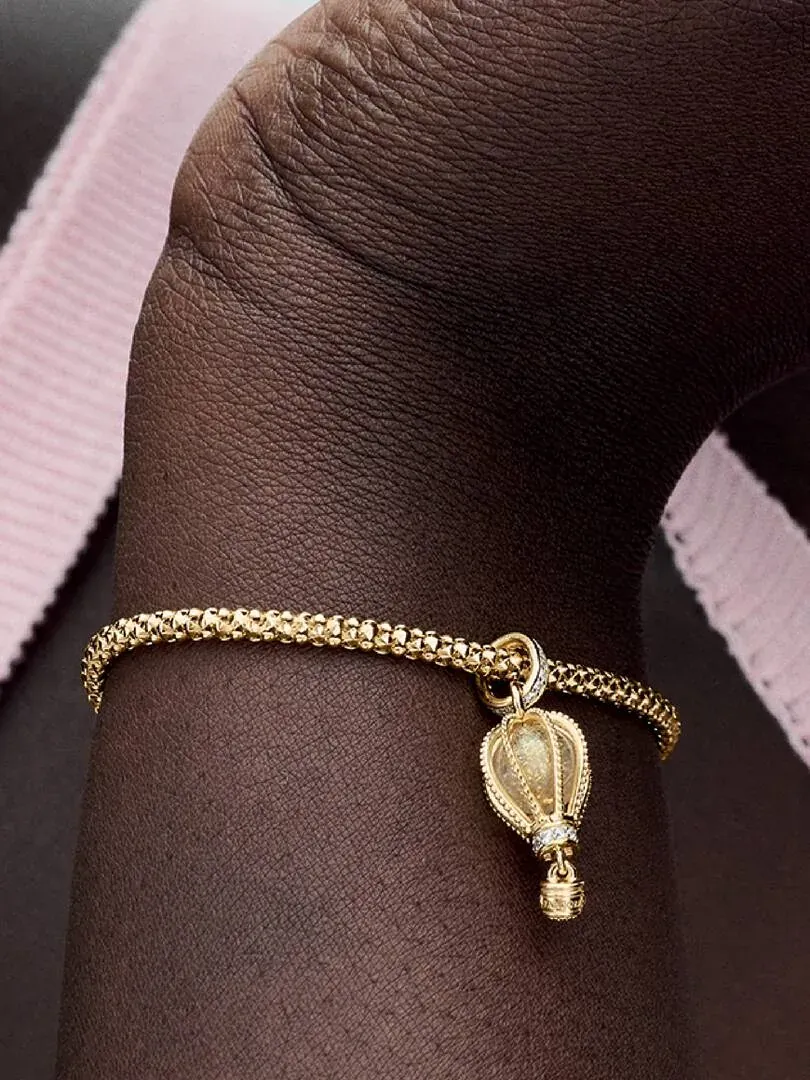 Nahaufnahme des Heißluftballon-Anhängers an einem Armband, getragen auf der Haut vor unscharfem rosa Hintergrund.