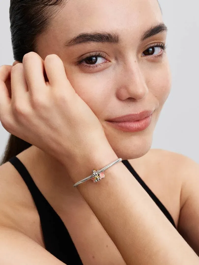 Primer plano del charm en la muñeca de una modelo, toma lateral con fondo neutro desenfocado.