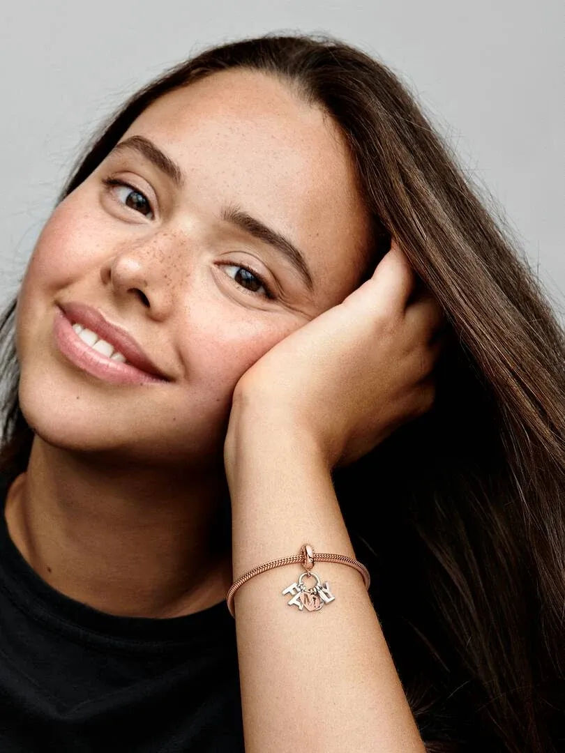 Primer plano de la muñeca con el charm de letras, modelo apoyada en su mano sobre fondo neutro.