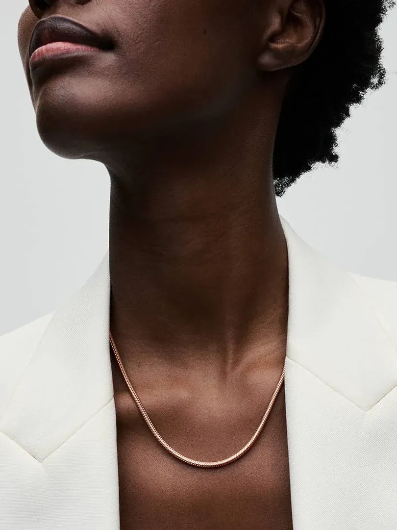 Primer plano del collar de cadena sobre el cuello de una modelo, con chaqueta blanca, ángulo contrapicado.