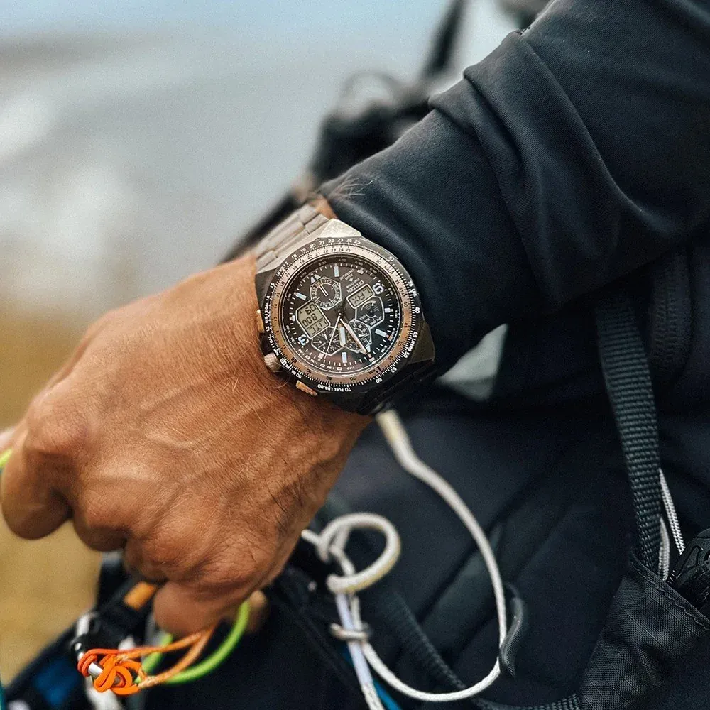 Reloj puesto en muñeca masculina con chaqueta negra y cuerdas de escalada, fondo exterior desenfocado.