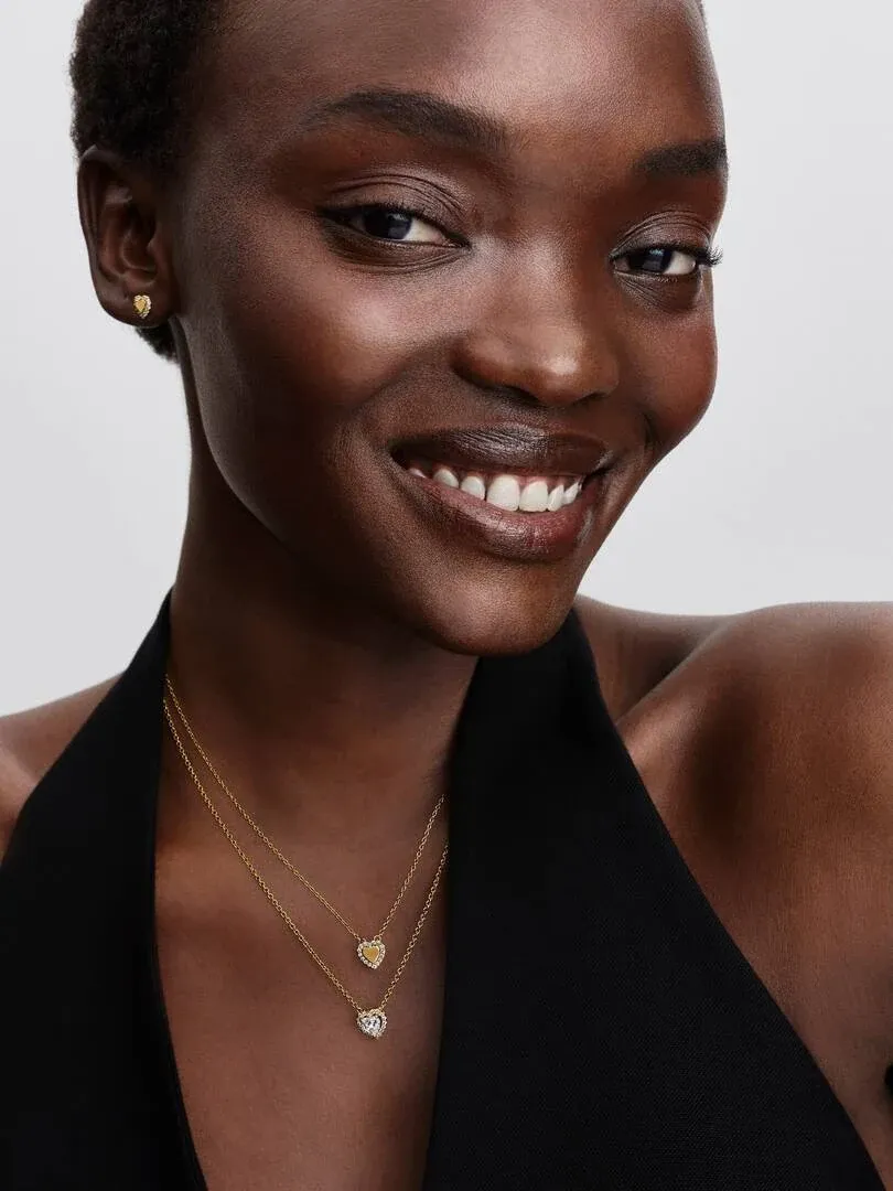 Gros plan du collier avec pendentif cœur doré sur le cou, vue de face avec modèle sur fond blanc.