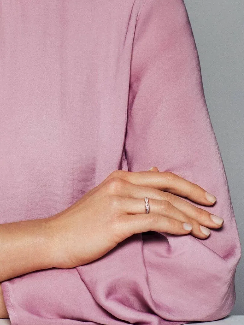 Primer plano del anillo en el dedo anular, sobre mano con blusa de seda rosa, toma lateral.